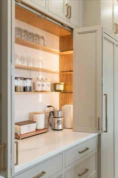 a kitchen with white cupboards and wooden shelves filled with glassware, tea kettle and coffee pot