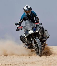 a man riding on the back of a motorcycle down a dirt road in the desert