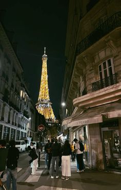 the eiffel tower is lit up at night, with people walking around it