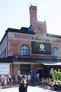 people walking in front of a brick building with many windows and plants on the outside