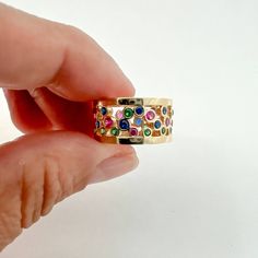 a hand holding a gold ring with multicolored stones on the inside of it