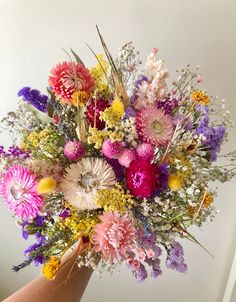 a hand holding a bouquet of flowers in it's left hand, with other flowers on the right