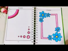 an open notebook with blue flowers and pink circles on the page, next to a flower arrangement