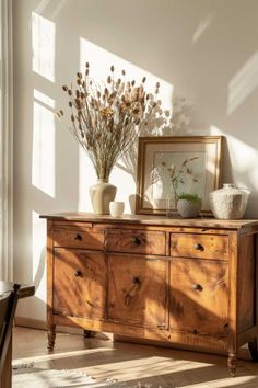 a wooden dresser with vases and plants on top of it in front of a window