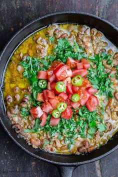 a skillet filled with beans, tomatoes and other vegetables on top of a wooden table