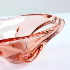 a pink glass bowl sitting on top of a white tablecloth covered table with an orange and brown swirl design