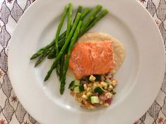 a white plate topped with asparagus and a piece of salmon on top of corn