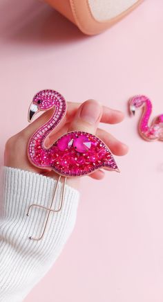 a pink flamingo brooch sitting on top of a woman's hand next to jewelry