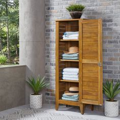 a wooden cabinet filled with lots of folded towels next to a brick wall and potted plants