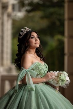 a woman in a green dress is holding flowers and looking off to the side while wearing a tiara