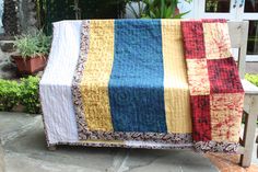 a quilted blanket sitting on top of a wooden bench next to potted plants