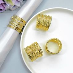 three gold rings sitting on top of a white plate next to a napkin and flowers