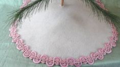 a close up of a pink crocheted doily with pine needles on it