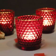 three red glass candles sitting on top of a table next to bananas and other items