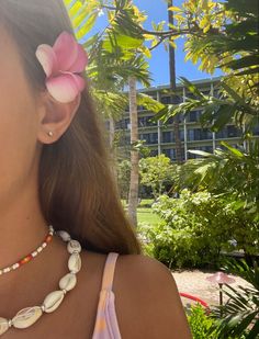 a woman wearing a pink flower in her hair with a shell necklace on it's neck