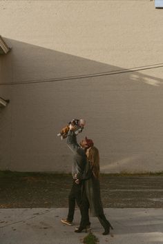 a man and woman walking down the street while holding their baby in one hand, looking at each other