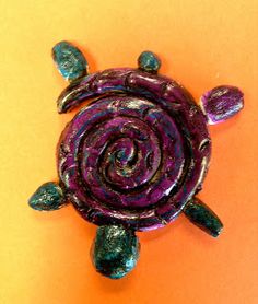 a purple and green turtle brooch sitting on top of an orange surface