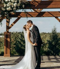 a bride and groom kissing under an arch with white flowers on the arbors at their wedding