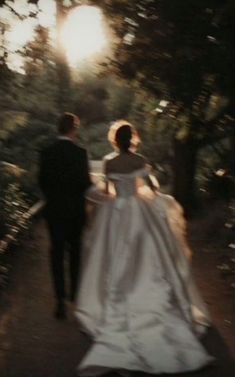 a bride and groom walking down a path in the woods at sunset or sunrise time