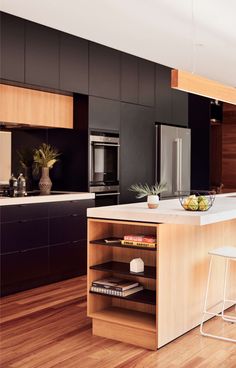 a kitchen with wooden floors and black cabinets is pictured in this image, there are two stools at the center of the island