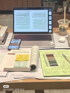 an open laptop computer sitting on top of a wooden table next to books and papers