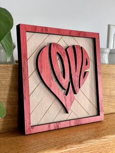 a wooden frame with a heart cut out of it on top of a table next to a potted plant