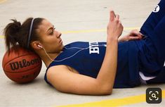 a woman laying on the ground next to a basketball and listening to headphones with ear buds