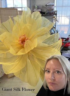 a woman standing in front of a giant yellow flower with the words giant silk flower on it