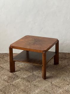 a small wooden table on a carpeted floor with a white wall in the background