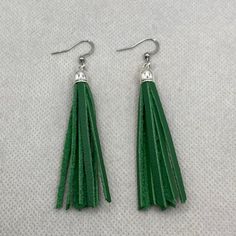 pair of green leather tassel earrings with silver hooks on white fabric background, closeup