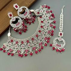 Ruby red polki bridal necklace set with beautiful jhumka earring and mangtika in silver rhodium finish. Inspire your style with this beautiful Indian bridal necklace set made with high quality reverse ad stone and pearl details to complete your look on your wedding day Earring length: 3.5 inch Earring width: 1.5 inch Mangtika Length: 7 inch Necklace length: adjustable length with dori closure. Create beautiful memory for any occasion with elegant jewelry for your loved ones You will receive carefully packaged items in jewelry box, ready to give memorable gift  to your Wife, mother, sister  friend or colleague. We will be happy to navigate you through the process so if you have any questions regarding our product before placing an order reach out to us and we will be there to help you.  Tha Silver Kundan Chandbali Bridal Sets, Silver Meenakari Chandbali Bridal Set, Silver Ruby Jewelry Sets For Festivals, Traditional Silver Kundan Necklace With Ruby, Silver Kundan Necklace With Ruby For Festivals, Festive Silver Kundan Necklace With Ruby, Punjabi Necklace, Necklace Set Silver, Silver Jhumkas