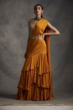 A vibrant pre-stitched layered saree with an embroidered cutwork belt. The saree is paired with a pearl, sequins, tilla & mirror work hand embroidered blouse. The sleeves have pearl & sikka... Luxury Pre-draped Saree With Mirror Work For Diwali, Luxury Traditional Wedding Dress With Drape, Luxury Yellow Bollywood Pre-draped Saree, Luxury Bollywood Pre-draped Yellow Saree, Luxury Bollywood Yellow Pre-draped Saree, Luxury Traditional Saree With Latkans, Drape Lehenga, Bhumika Sharma, Drape Saree