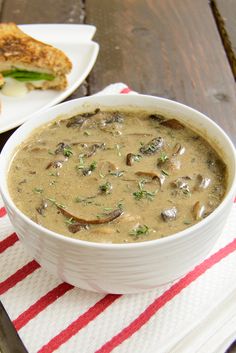 a bowl of mushroom soup on a red and white striped napkin with a sandwich in the background