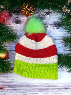 a crocheted hat with a green pom - pom sits on top of a pine tree