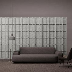 a gray couch sitting in front of a wall with squares on it and a lamp next to it