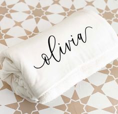 a white blanket with the word alvia on it sitting on top of a patterned floor