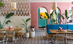 the interior of a restaurant with blue and pink booths, wooden tables, and potted plants