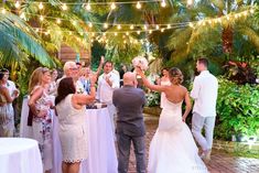 a bride and groom are dancing at their wedding reception in the tropical garden with string lights strung across the walkway