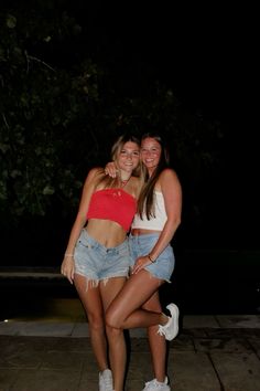 two young women posing for the camera in front of a tree at night with their arms around each other