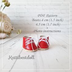 a pair of red baby shoes sitting on top of a white table next to flowers