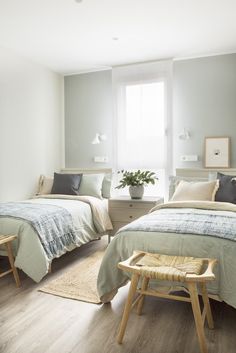 two beds in a bedroom with white walls and wood floors, one has a plant on the end table