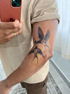 a man with a bird tattoo on his arm holding a cell phone and taking a selfie