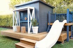 a small house with a slide and potted plants on the front porch, next to a deck