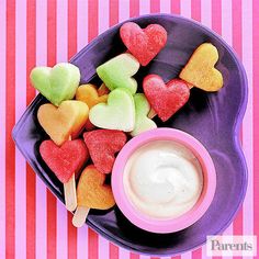 heart shaped candies and dip in a bowl on a purple plate with pink stripes