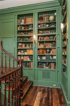 a green bookcase in the corner of a room with stairs and bookshelves