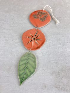 three ceramic ornaments with designs on them sitting on a white table top, one has a green leaf and the other is an orange flower