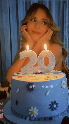 a woman sitting in front of a blue cake with two lit candles on the top