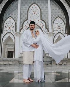 a man and woman standing in front of an ornate building with white curtains on it