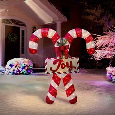 a lighted candy cane in front of a house with the word joy written on it