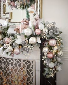 a christmas wreath with pink and silver ornaments hanging from it's sides next to a fireplace